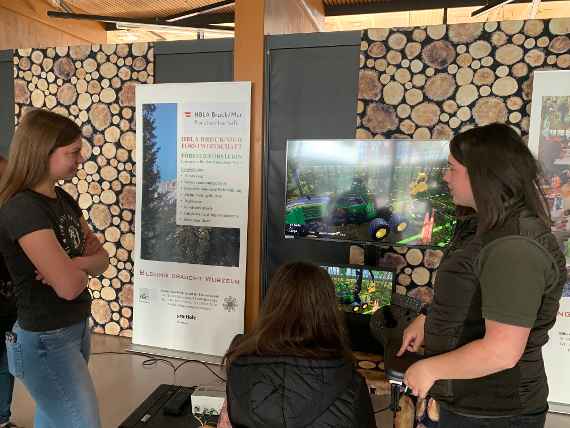 Schülerinnen und Besucherin vor dem Harvestersimulator und Plakaten