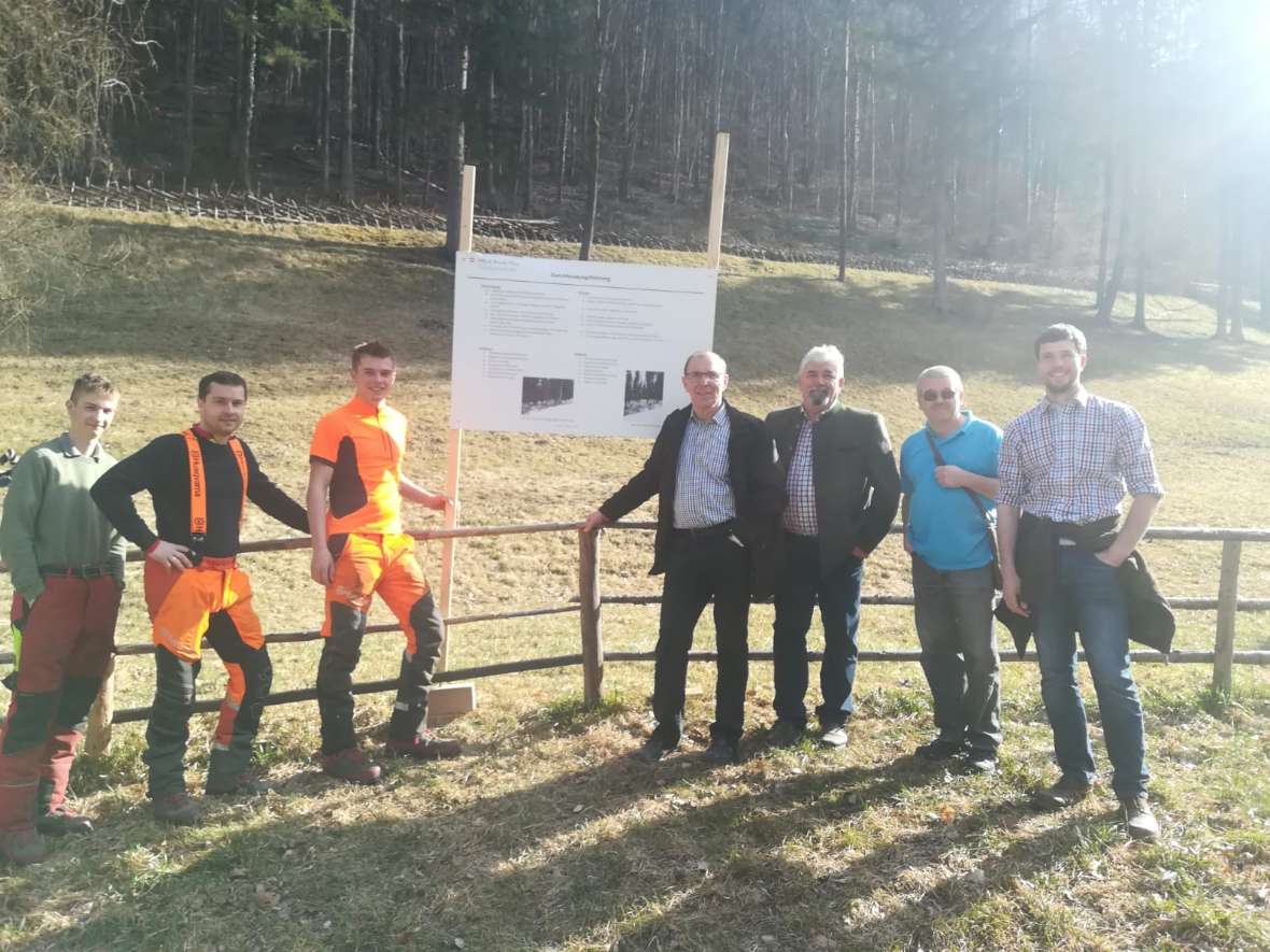 Eine Gruppe von Besuchern mit Schülern auf einer Wiese vor Zaun